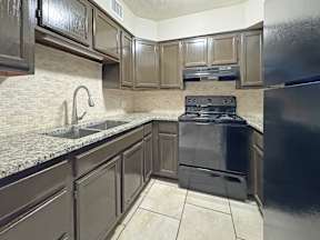 Kitchen with dark cabinets, granite-look counters, and black appliances at Los Cedros Apartments