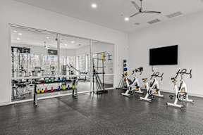 A room with a black floor and white walls has exercise bikes and a television.