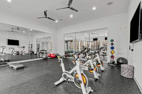 A gym with a row of stationary bikes and a television on the wall.