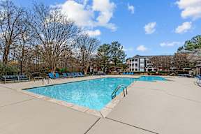 A large swimming pool surrounded by trees and chairs.