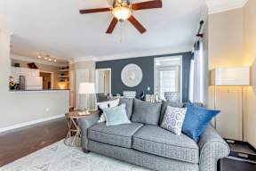 A grey couch with blue pillows is in the center of a room with a ceiling fan.