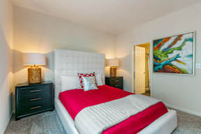 A bedroom with a red bedspread and a white headboard.