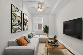 A living room with a grey couch, a coffee table, a ceiling fan, and a flat screen TV mounted on the wall.