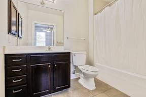 A white toilet sits in a bathroom with a white shower curtain.