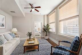 A living room with a white couch, a blue chair, and a ceiling fan.