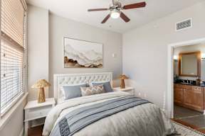 A bedroom with a large bed, a ceiling fan, and a painting of a mountain landscape on the wall.