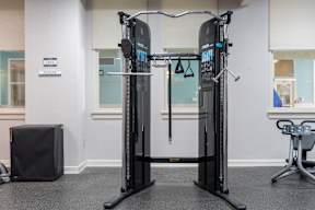 A black and grey gym machine sits in a room with a grey floor and white walls.