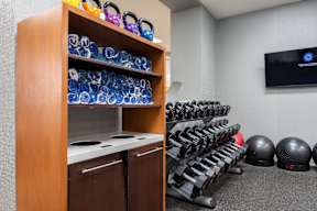 A gym room with a row of kettlebells and a rack of blue kettlebells.