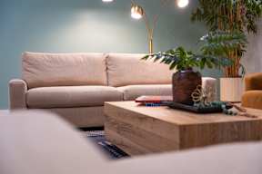 A beige couch sits in a living room with a wooden coffee table in front of it.