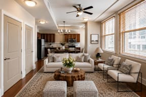 A well-lit living room with a ceiling fan and a kitchen in the background.