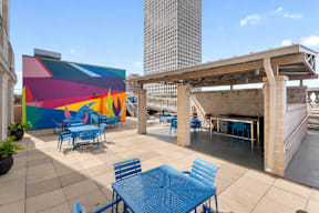 A colorful mural on a building with blue tables and chairs in front.