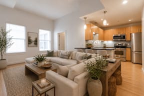 A modern living room with a large couch, a coffee table, and a kitchen in the background.