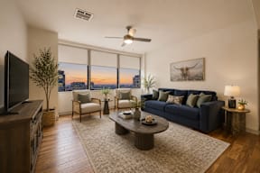 A living room with a large window overlooking the city at sunset.