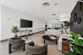 A modern living room with a grey sofa, a grey armchair, a black coffee table, and a television on the wall.