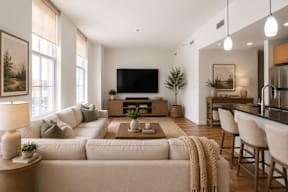 A modern living room with a large couch, a flat-screen TV, and a kitchen area in the background.