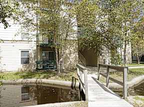 A small wooden bridge over a pond in front of a building.