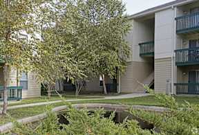 A tree in front of a building with a green railing.