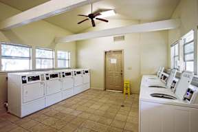 A room with a row of washing machines and a ceiling fan.