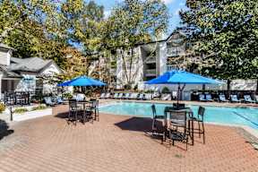 A pool area with chairs and umbrellas is surrounded by trees. at The Point at Perimeter, Georgia, 30338