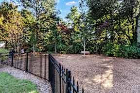 A black metal fence surrounds a dirt area with trees in the background. at The Point at Perimeter, Georgia, 30338