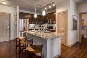 A kitchen with a granite countertop and wooden chairs.