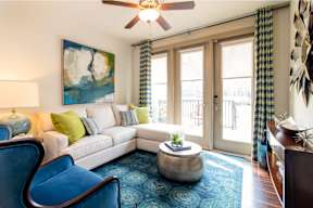 A living room with a white couch, blue chairs, and a painting on the wall.