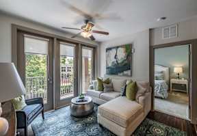 A well-lit living room with a ceiling fan and a view of the balcony.