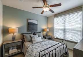 A bedroom with a bed, two lamps, and a ceiling fan.