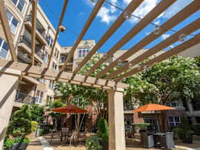 A patio with a pergola and umbrellas is surrounded by apartment buildings.