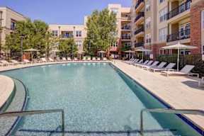 A large swimming pool surrounded by sun loungers and apartment buildings.