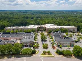 A large white building is surrounded by smaller buildings and trees.