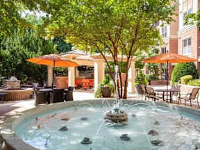 A fountain in the middle of a courtyard surrounded by trees and chairs.