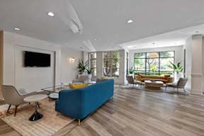 A blue sofa sits in a spacious living room with a television mounted on the wall.