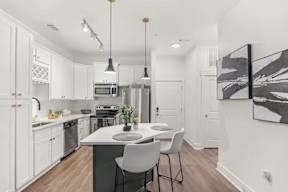 A kitchen with white cabinets and a black and white painting on the wall.