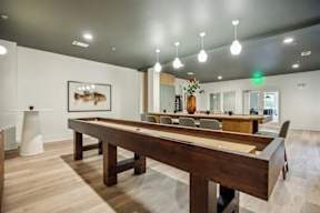 A long wooden table is in the middle of a room with a white wall and a painting hanging on it.