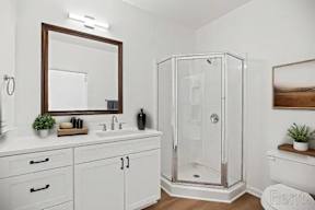 A white bathroom with a mirror, sink, and shower.