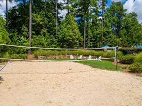 A sandy volleyball court surrounded by trees and a fence.