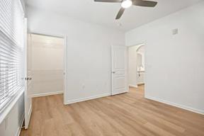 A room with a ceiling fan and light, wooden floors, and white walls.