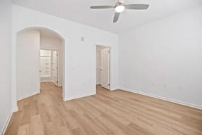 A room with a ceiling fan and light, hardwood floors, and white walls.