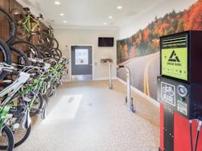 A bike rack with many bikes parked in front of a green recycling bin.