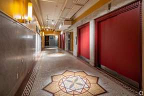 A long hallway with a tiled floor and a rug with a flower design in the middle.