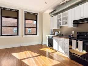 A kitchen with white cabinets and wooden floors.