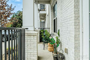 A white house with a black gate and plants on the porch.