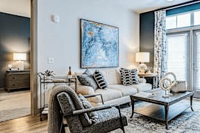 A modern living room with a grey chair, a white sofa, and a large painting on the wall.