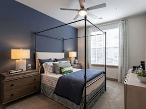 A bedroom with a four-poster bed, a ceiling fan, and a nightstand with a lamp.