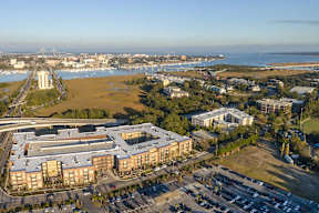 A large building complex is surrounded by a parking lot and a body of water.