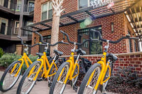 A row of yellow bicycles are parked in front of a brick building.