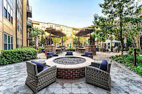 A patio with a fire pit surrounded by chairs and a building in the background.