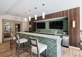 A kitchen with a green backsplash and a bar area with two chairs.