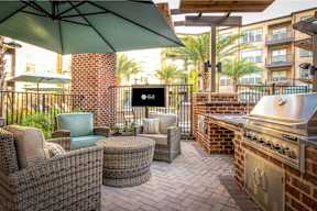 A patio with a grill and chairs under an umbrella.